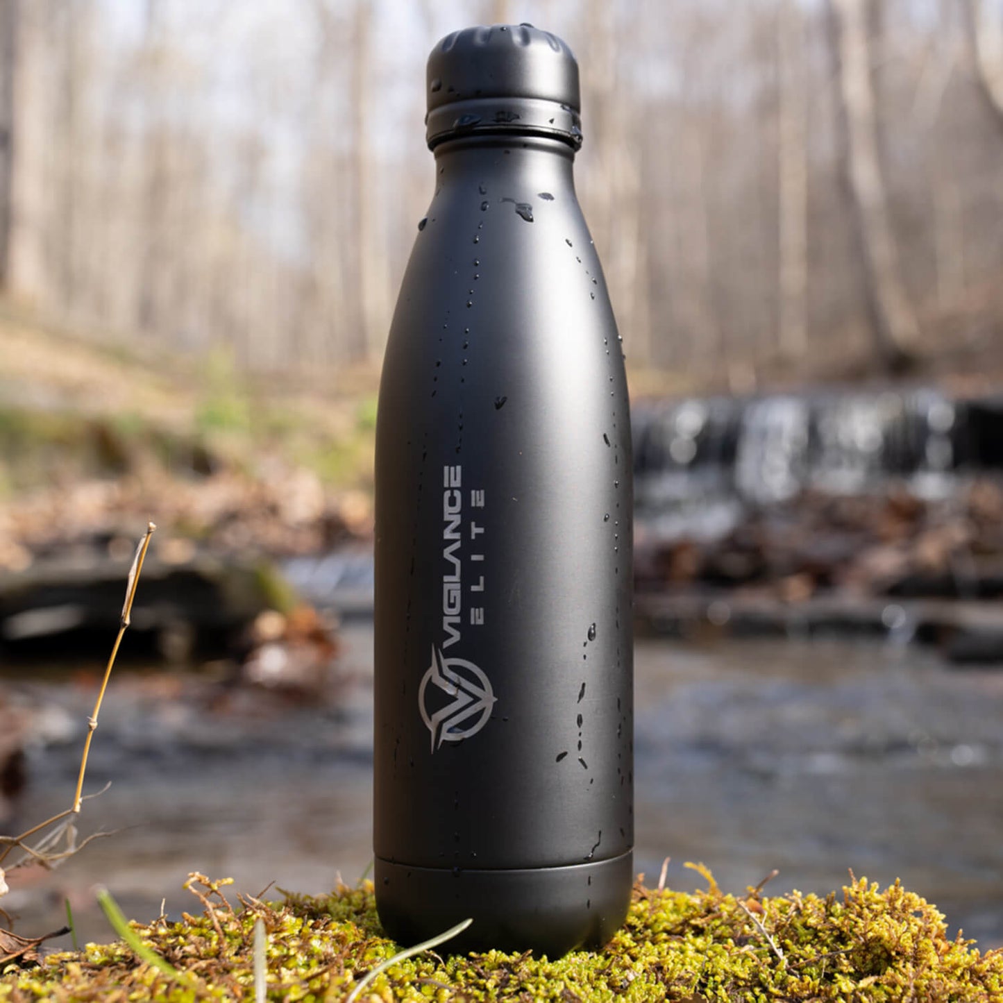 Black Vigilance Elite Beverage Bottle in the sun sitting on moss.